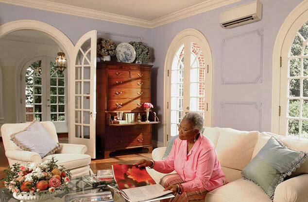 Woman in her living room with a wall-mounted ductless unit in the room