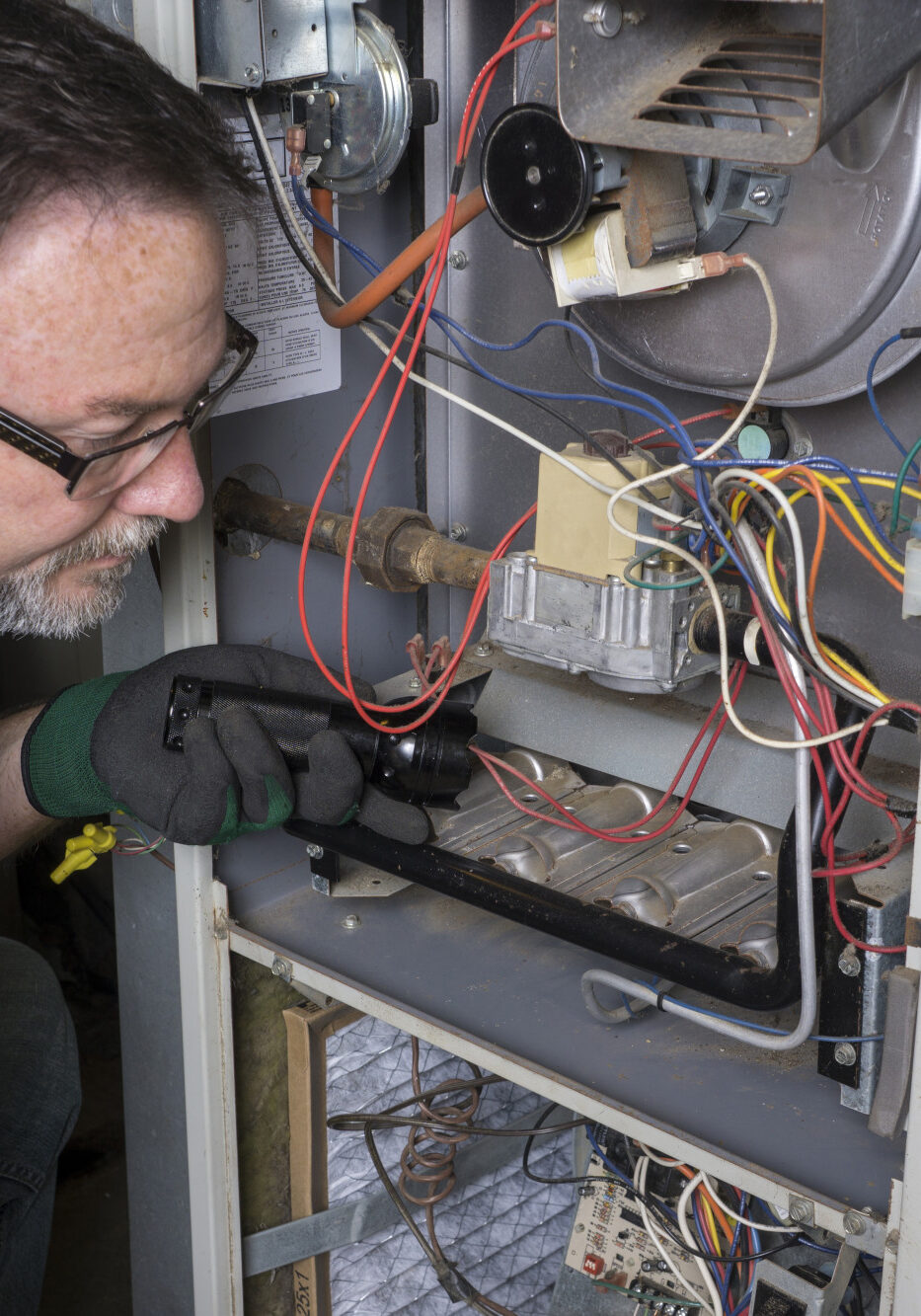 Techician looking over a gas furnace with a flashlight before cleaning it.